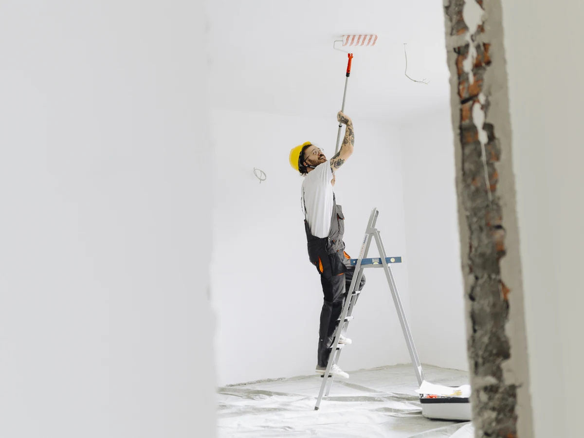 Painter on ladder using roller on ceiling with proper access equipment